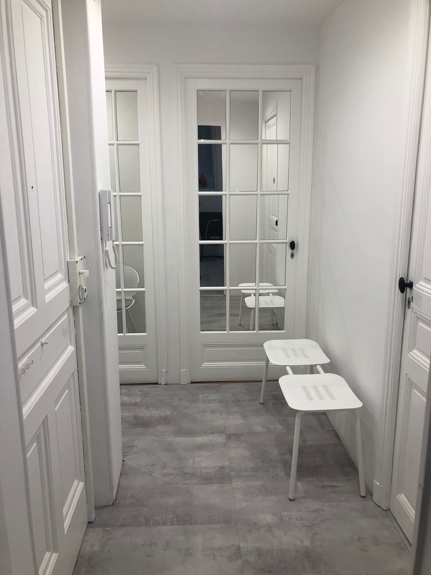 Étroit couloir blanc avec des portes-fenêtres et un petit banc blanc contre le mur de droite.