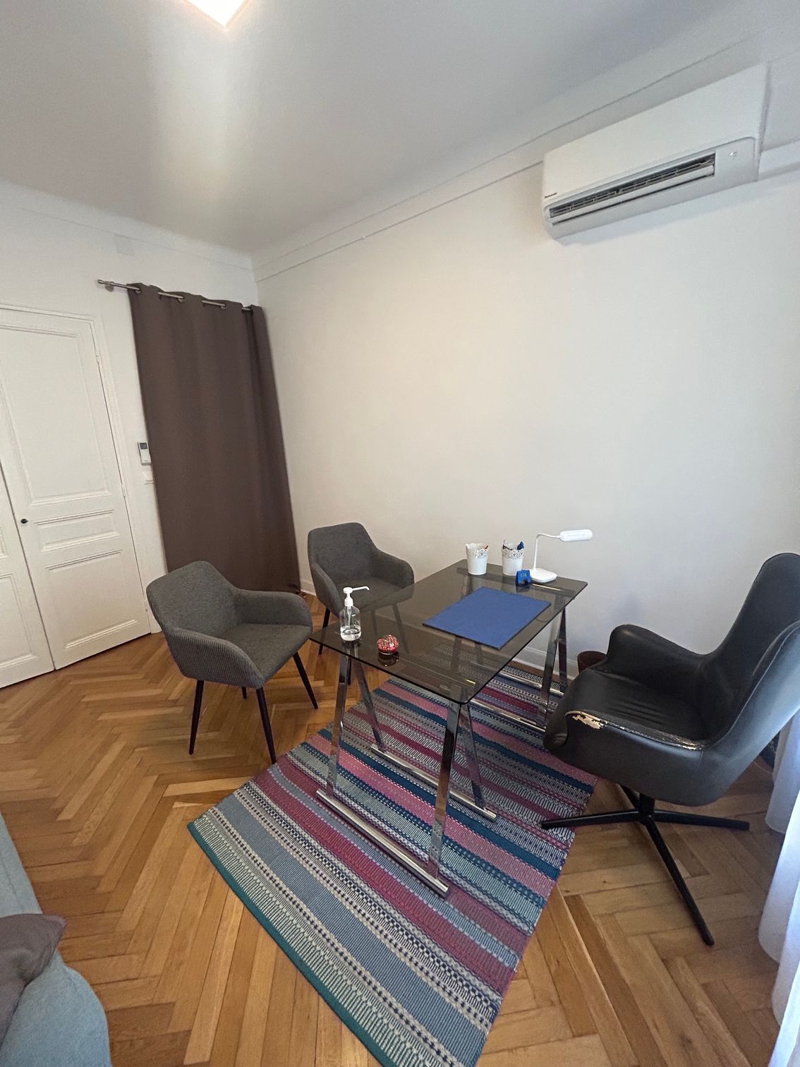 Petit salon avec des fauteuils, une table basse, un tapis à rayures, des rideaux et un climatiseur mural.