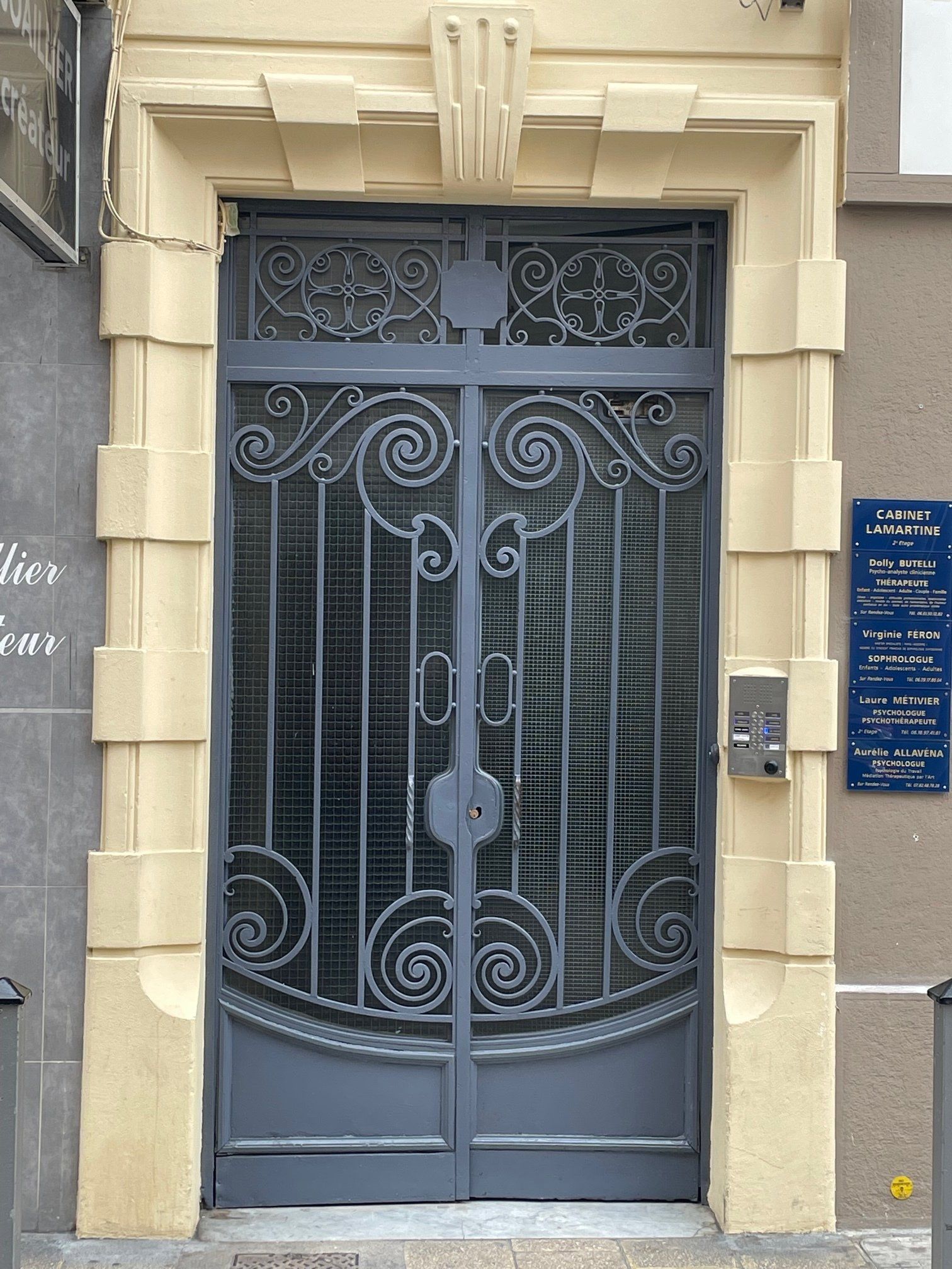 Porte bleue ouvragée en fer forgé, intégrée dans une façade en pierre beige