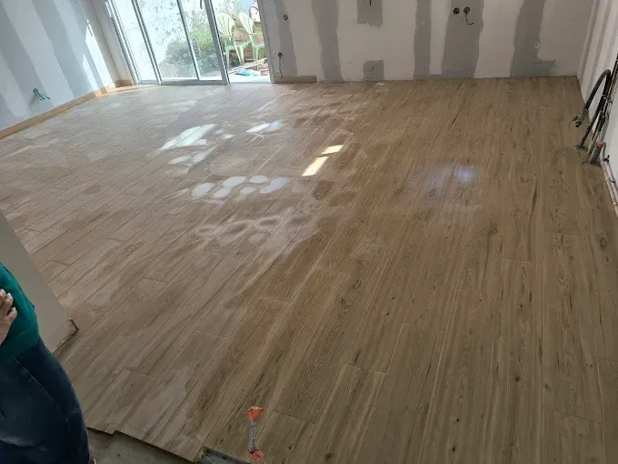 Pièce vide avec parquet clair récemment installé et lumière du soleil inondant les grandes fenêtres.