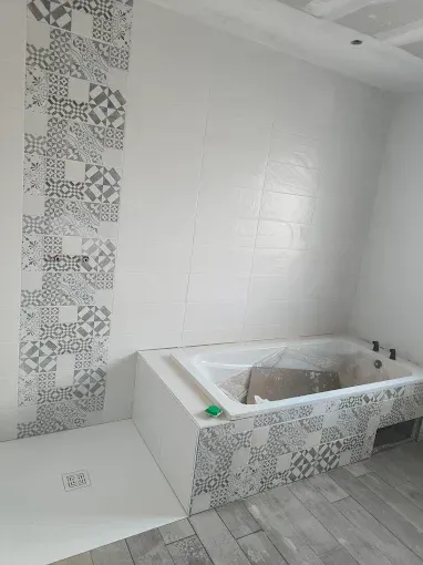 Salle de bains avec murs carrelés blancs, carreaux décoratifs à motifs et baignoire encastrée en construction.