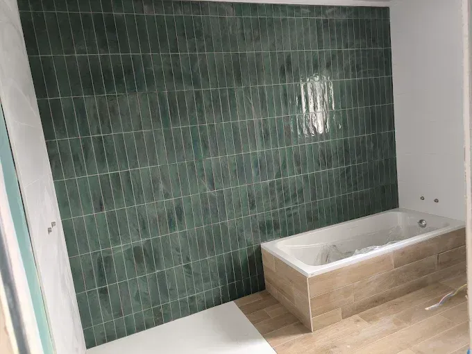 Petite salle de bains en construction avec un mur carrelé vert et une baignoire beige
