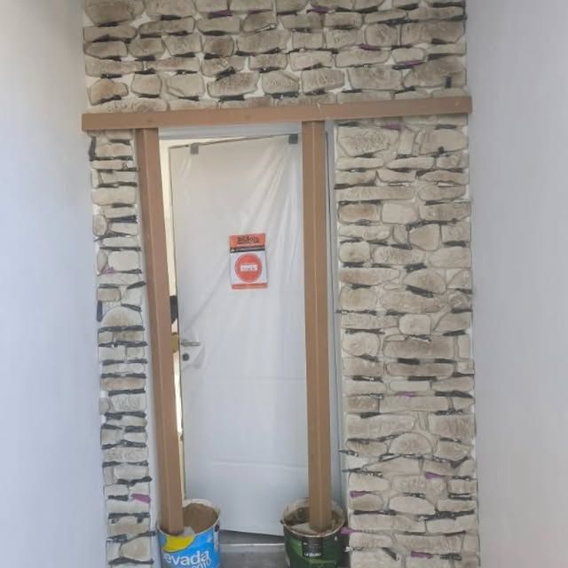 Mur en pierre avec une porte blanche et un panneau d'avertissement, encadré par des boiseries brutes.