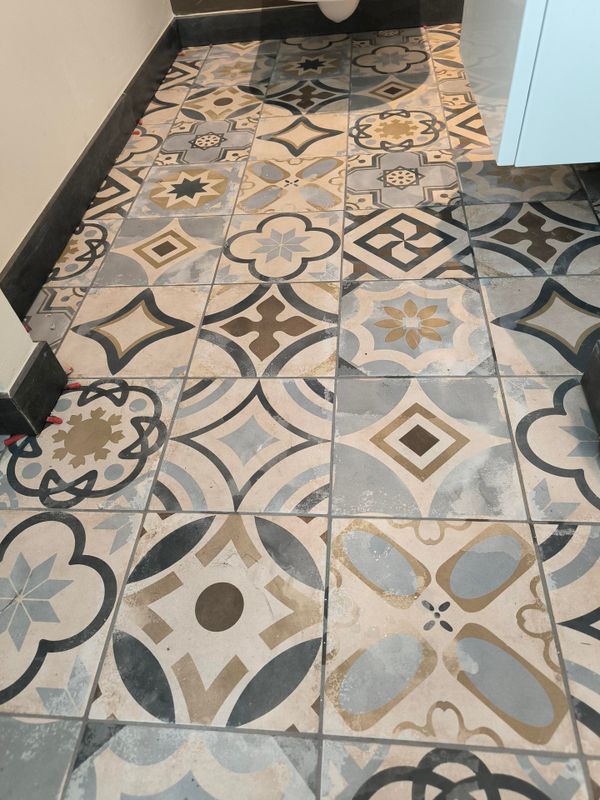 Sol carrelé à motifs géométriques et floraux gris, crème et bleus dans un couloir