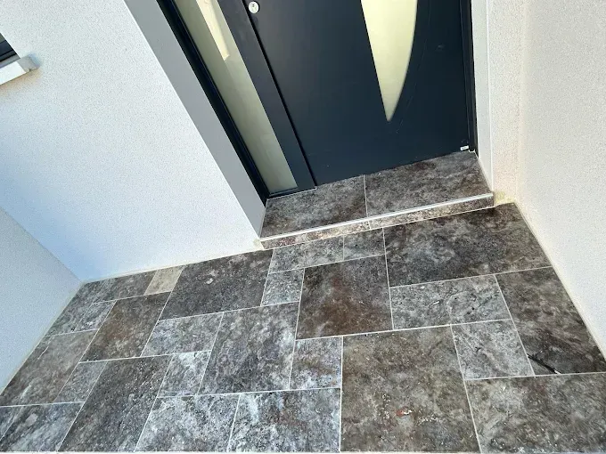 Sol carrelé dans l'entrée menant à une porte d'entrée sombre avec un panneau en verre dépoli