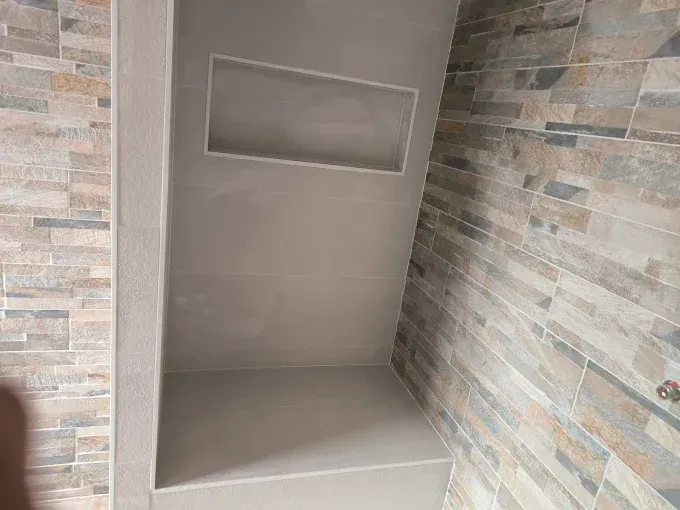 Cabine de douche carrelée vide avec étagère intégrée et niche encastrée.