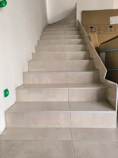 Escalier intérieur carrelé avec des marches beiges et un mur blanc, menant à un étage supérieur à côté de cartons.