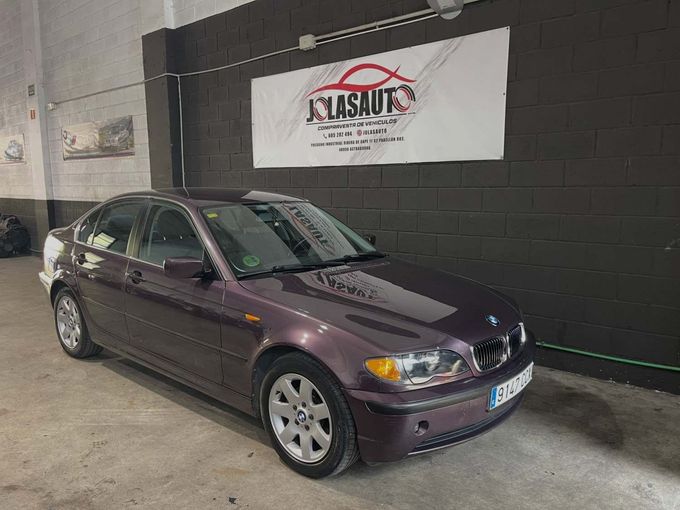 Sedán morado estacionado en el interior, junto a una pared negra y una pancarta blanca.