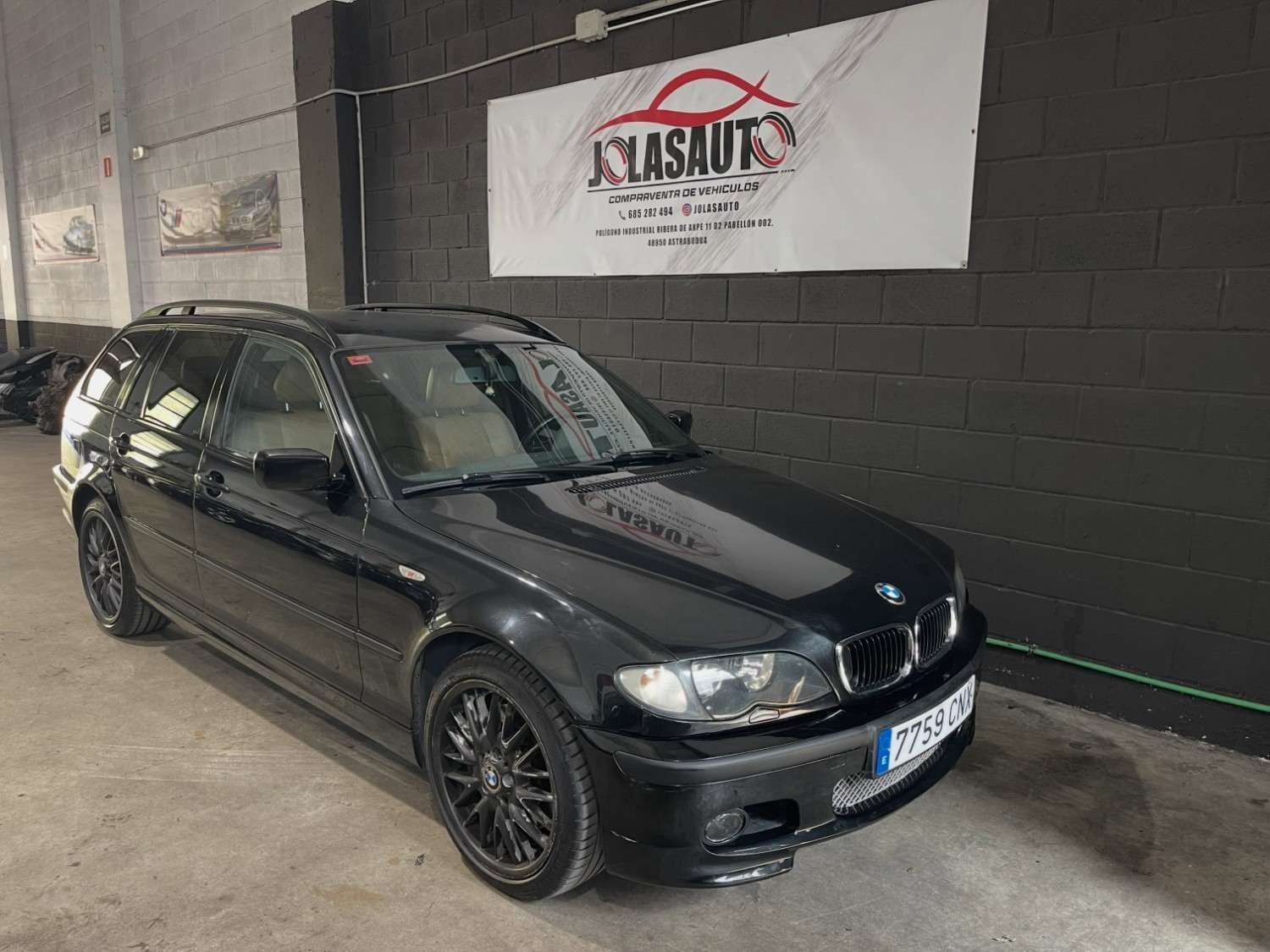 Sedán BMW negro estacionado en el interior junto a una pared con una pancarta.