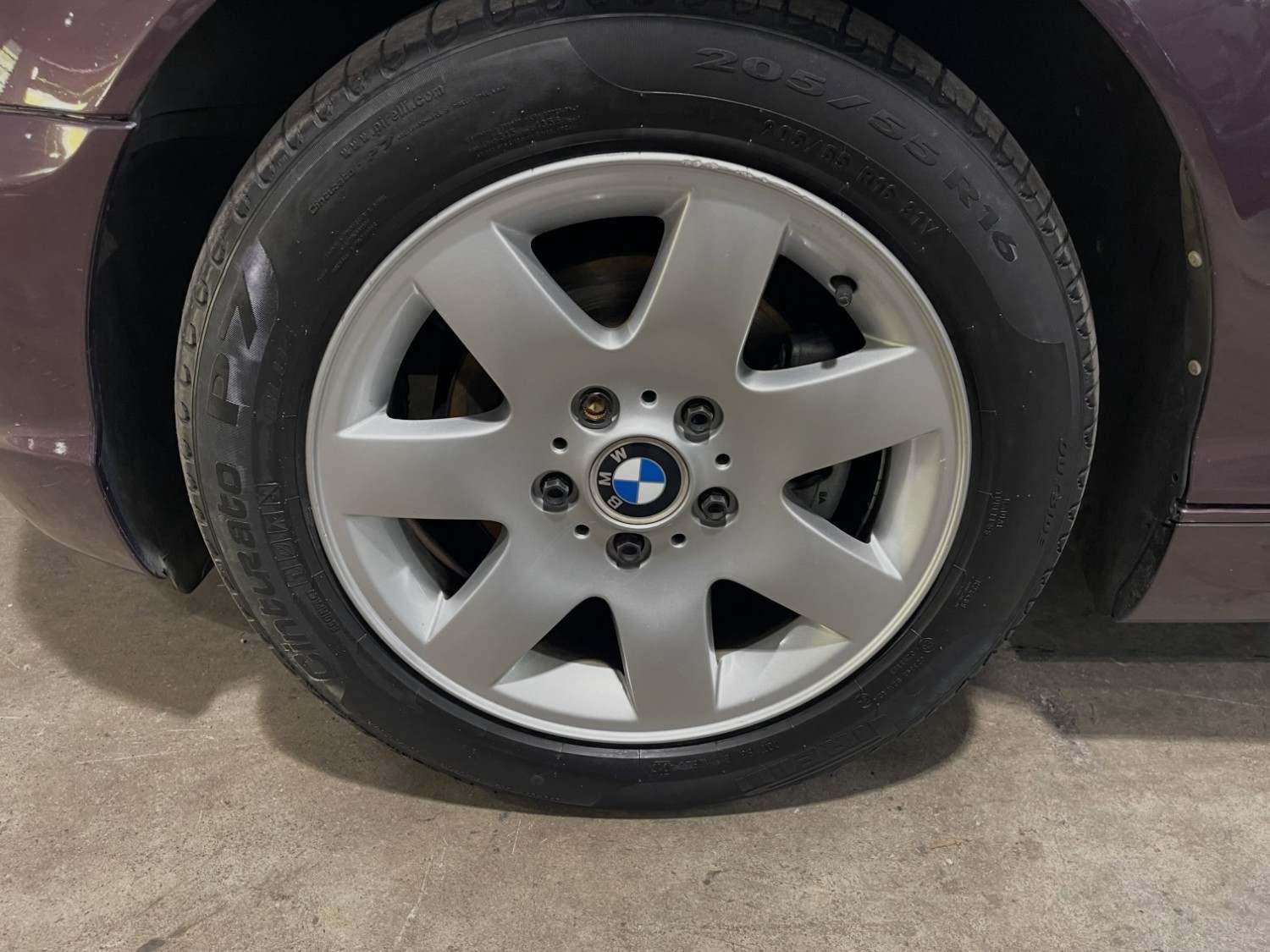 Primer plano de una rueda de coche con llanta de aleación plateada y el logotipo de BMW sobre un suelo de hormigón.