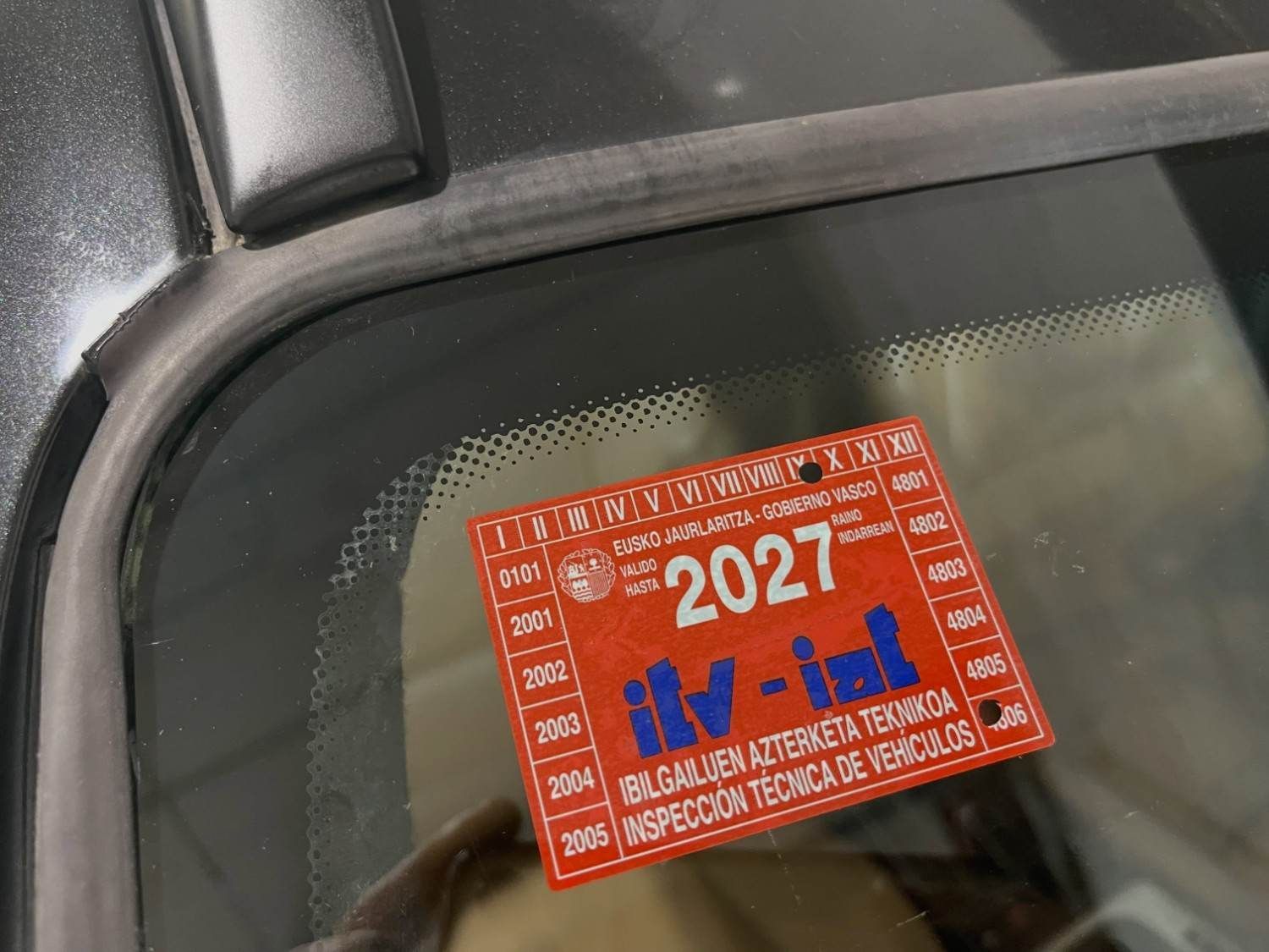 Pegatina roja de inspección vehicular de 2027 en el parabrisas de un coche, cerca del retrovisor