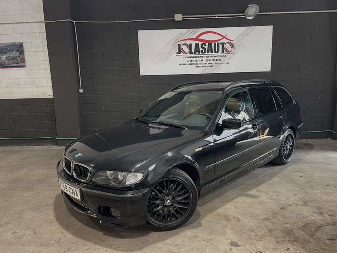 BMW familiar negro con llantas de repuesto aparcado en el interior, frente a una pancarta en la pared