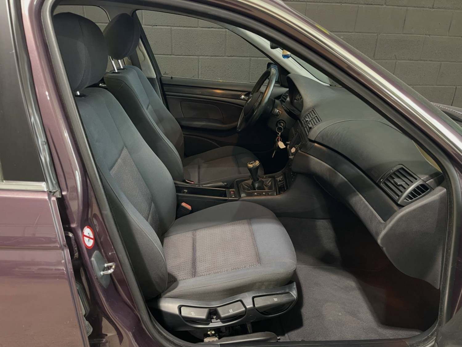 Interior del coche con asientos negros y la puerta del conductor abierta, con el habitáculo delantero y el salpicadero a la vista