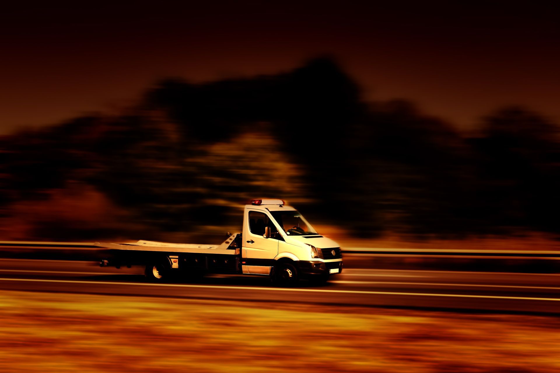 Dépanneuse filant à toute allure sur l'autoroute, mouvement flou. Ciel sombre, arbres en arrière-plan.