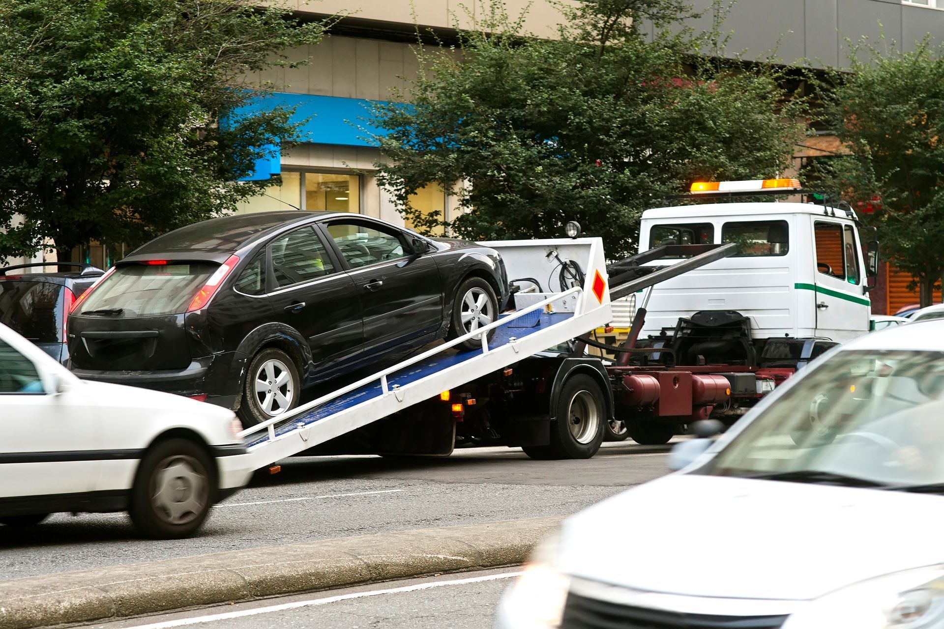Une voiture noire est remorquée par une dépanneuse dans une rue de la ville.
