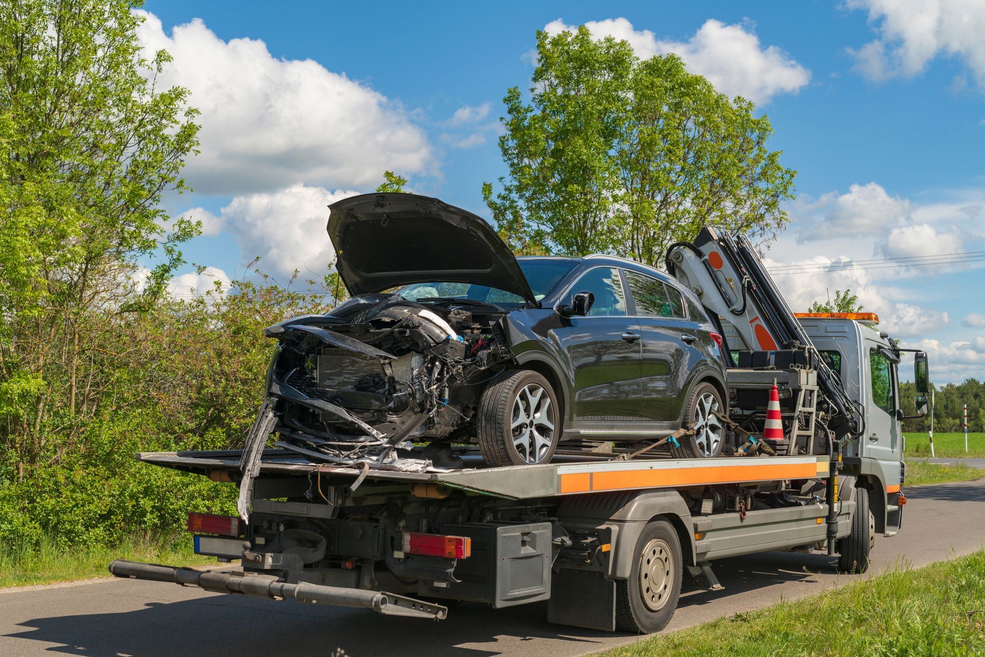 Voiture noire endommagée sur une dépanneuse, l'avant écrasé, le capot ouvert, garée en bord de route.