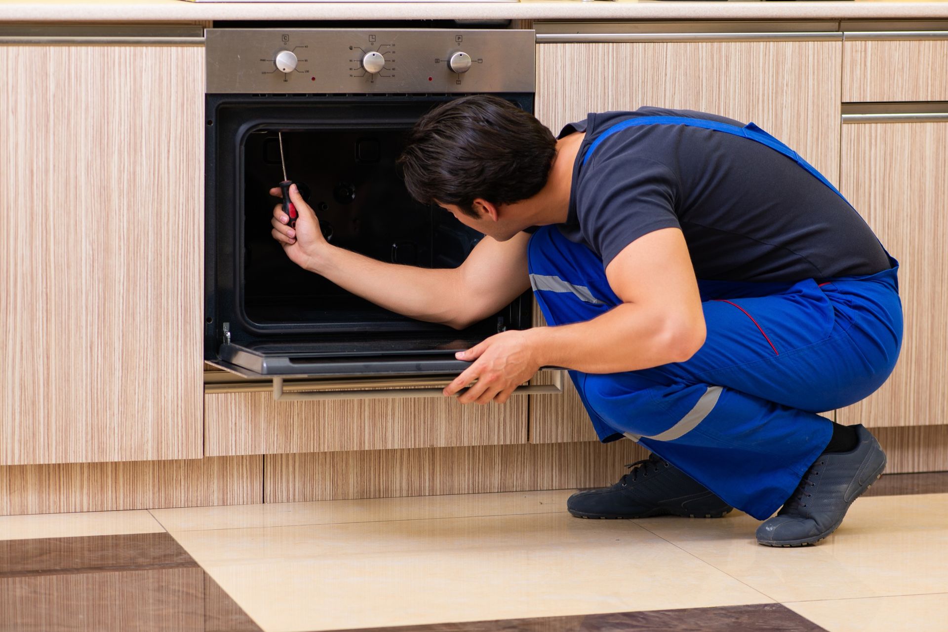 Un hombre está arreglando un horno en una cocina con un destornillador.