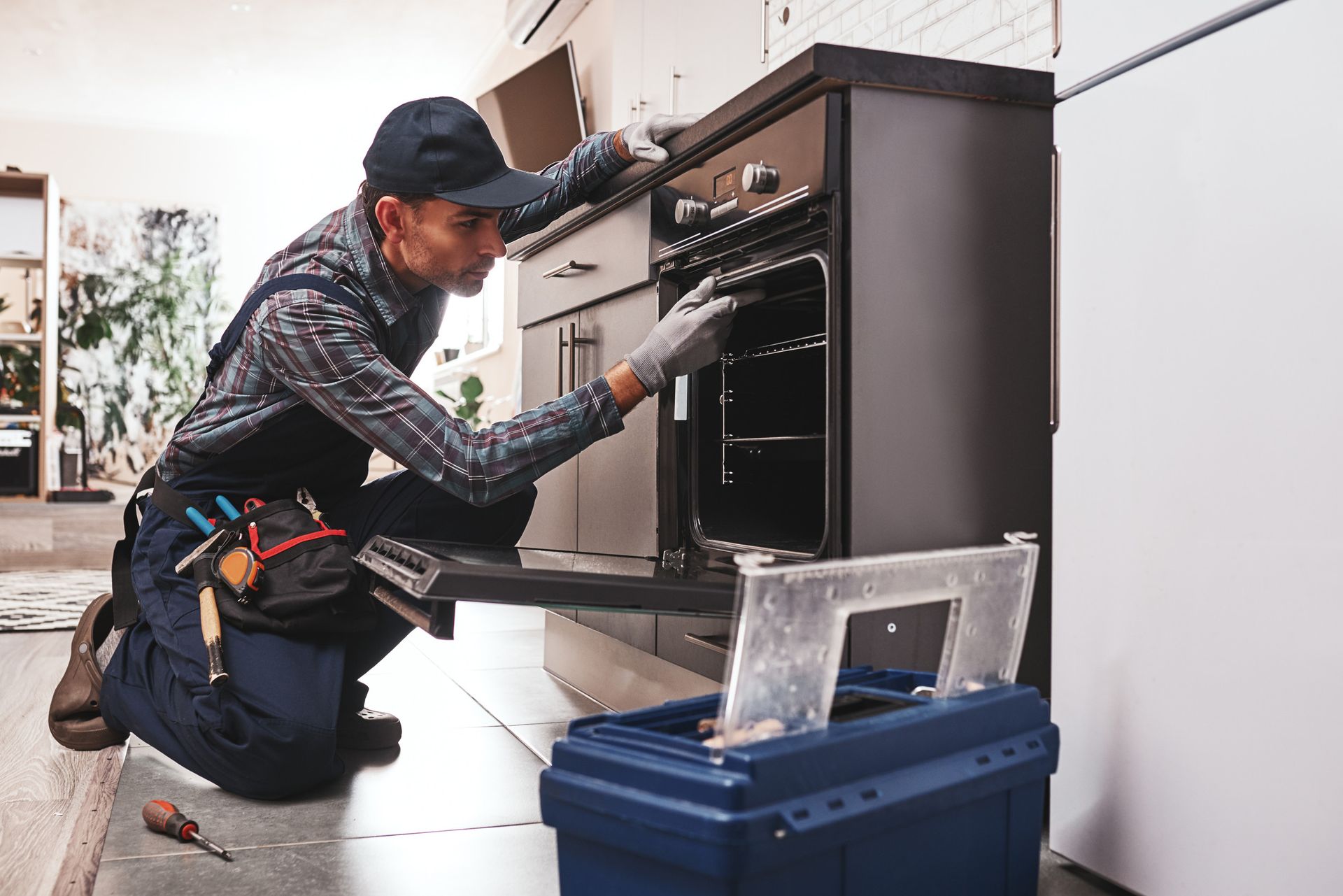 Un hombre está arrodillado en una cocina arreglando un horno.