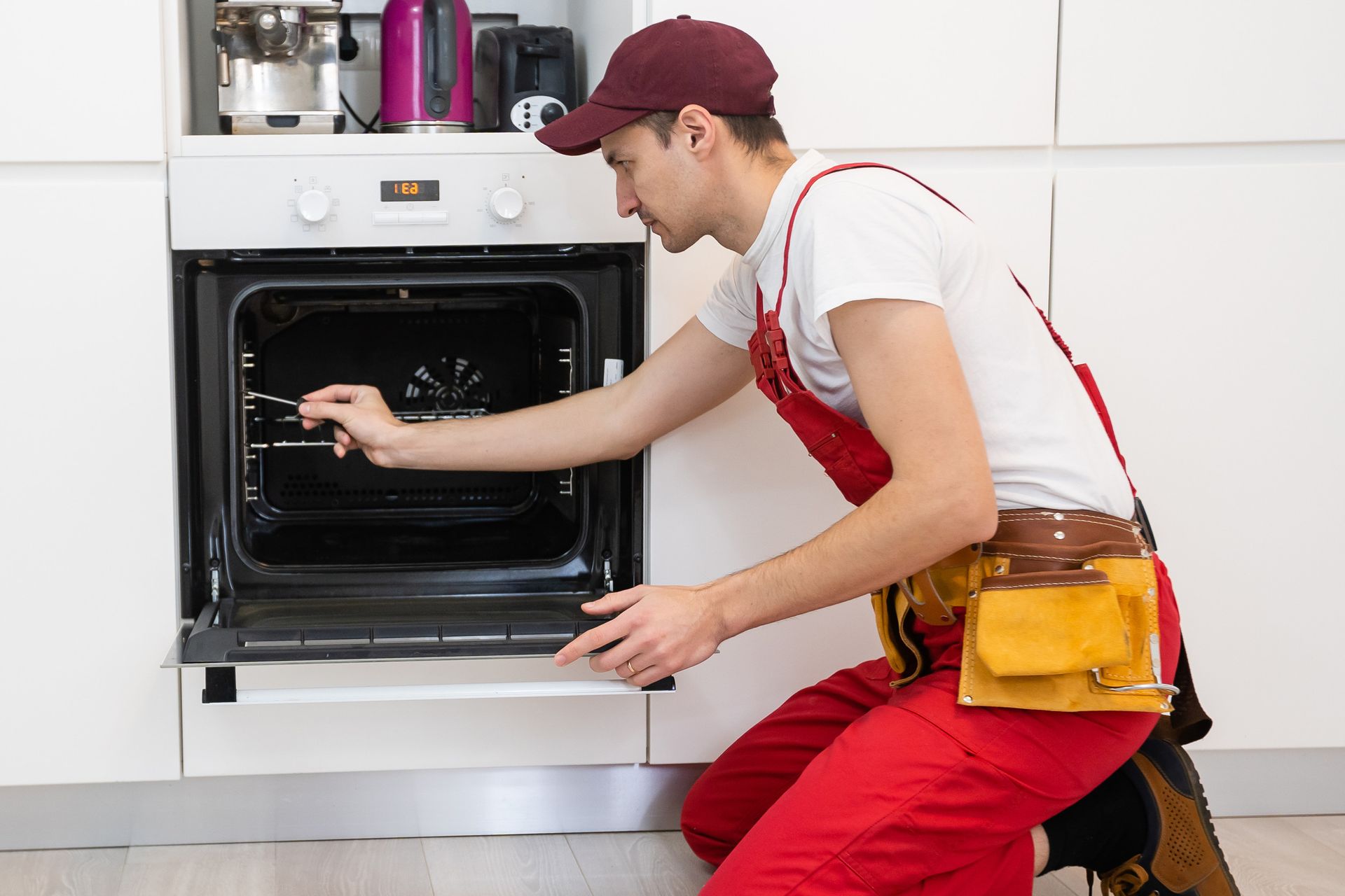 Un hombre está arreglando un horno en una cocina.