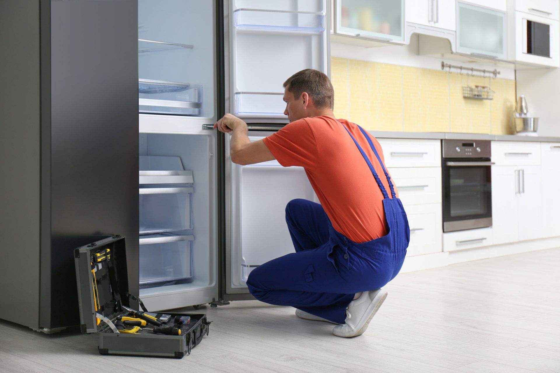 Un hombre está reparando un refrigerador en una cocina.