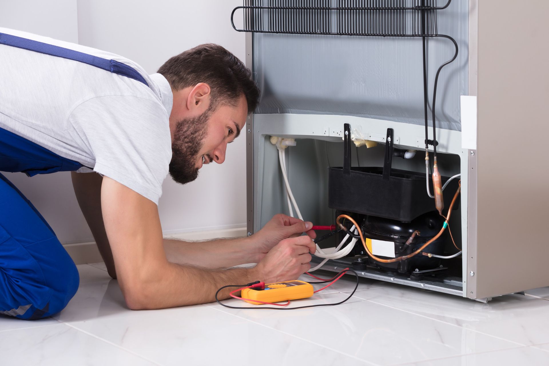 Un hombre está arrodillado en el suelo arreglando un refrigerador.