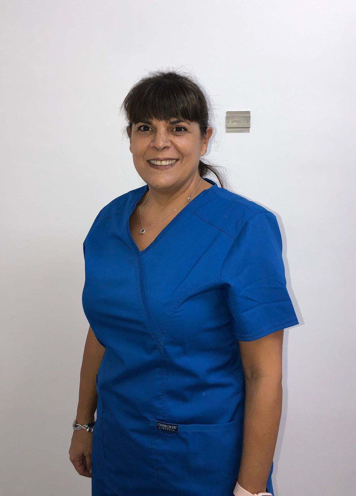 Una mujer con un uniforme azul sonríe y está parada frente a una pared blanca.