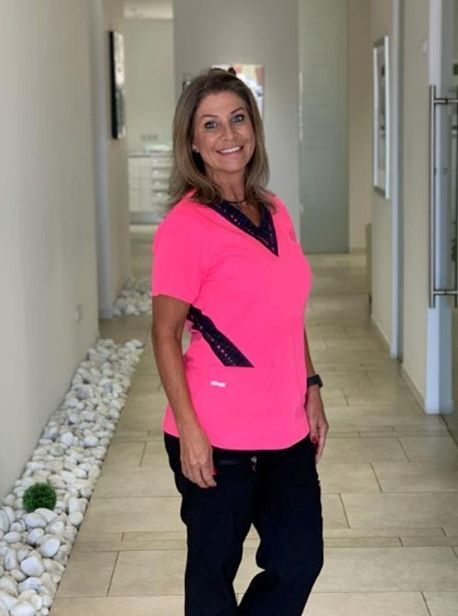 Una mujer con una blusa rosa y pantalones negros está parada en un pasillo.