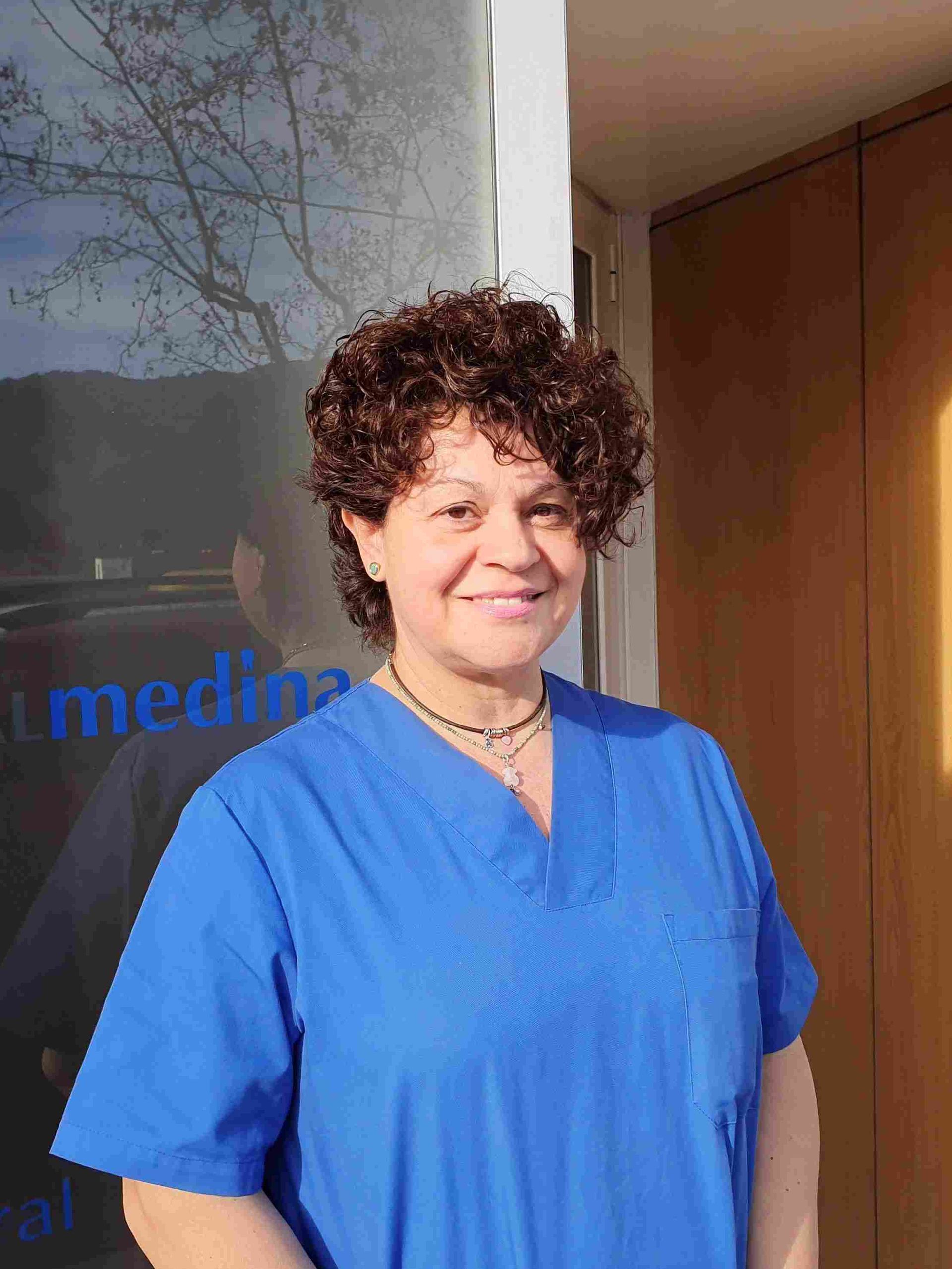 Una mujer con un uniforme azul sonríe frente a una ventana que dice medicina.