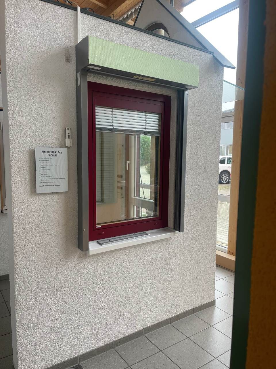 Ein Ausstellungsraum mit mehreren schrägen Dachfenstern, die an einem schwarzen, kantigen Rahmen über zwei beigen Sesseln angebracht sind.