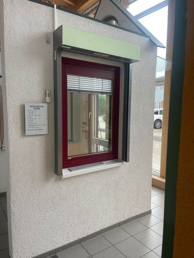 Ein rot umrahmtes Servicefenster mit hochgezogenem Fensterladen, angebracht an einer strukturierten, hellen Wand.