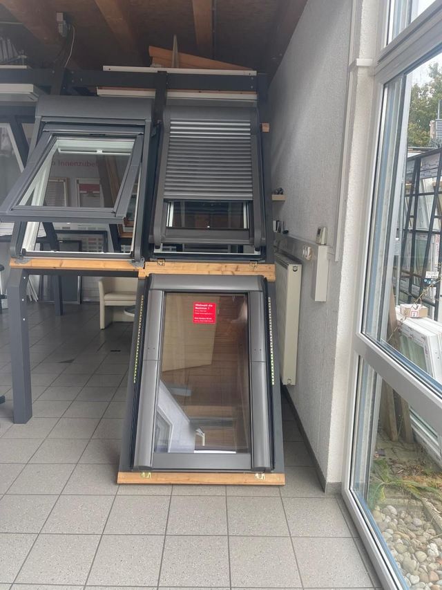 Ausstellung mehrerer Dachfenstermodelle mit grauen Rahmen in einem Ausstellungsraum mit Fliesenboden und Glaswand.