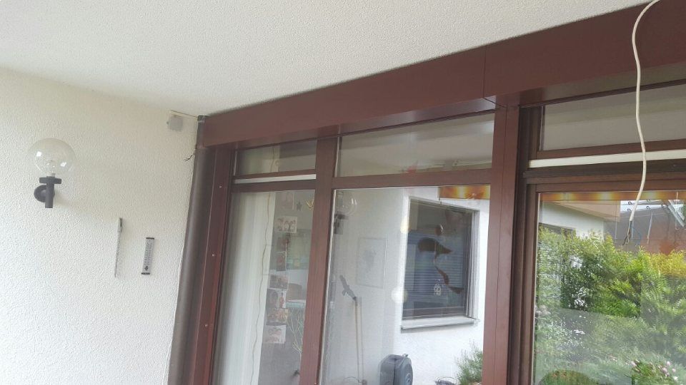Ansicht einer weißen Außenwand mit einer braun gerahmten Glasschiebetür und einer Außenleuchte.