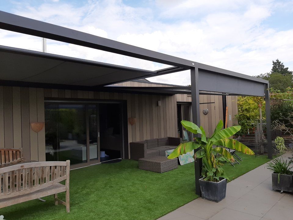 Eine moderne Außenterrasse mit ausfahrbarer Markise, Holzbank, Lounge-Garnitur auf Kunstrasen und Topfpflanze.
