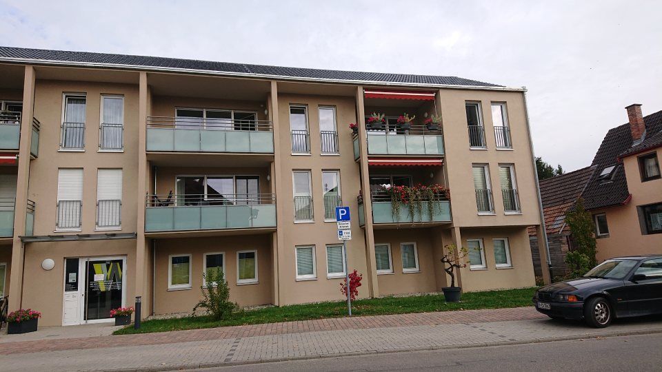 Ein modernes dreistöckiges Wohnhaus mit Balkonen, beigen Wänden und einem schwarzen Auto, das im Vordergrund geparkt ist.
