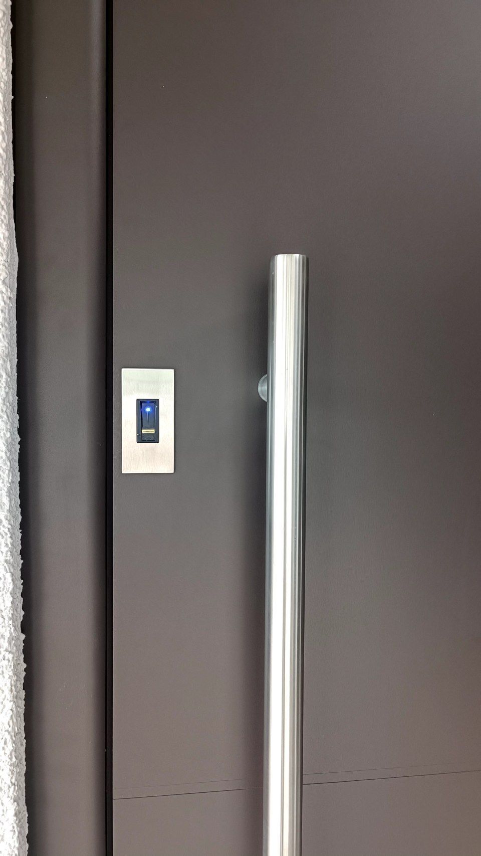 Eine dunkelgraue Tür mit einem vertikalen silbernen Türgriff und einem kleinen, rechteckigen silbernen elektronischen Zugangstastaturfeld.