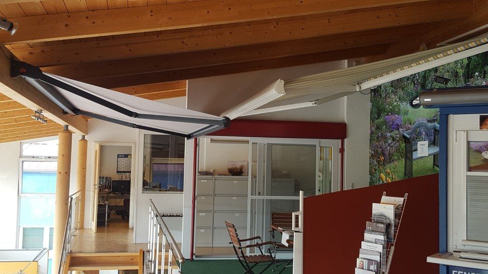 Eine breite, einziehbare Markise erstreckte sich teilweise über einen Terrassenbereich mit Holzdecke und einem Prospektständer.
