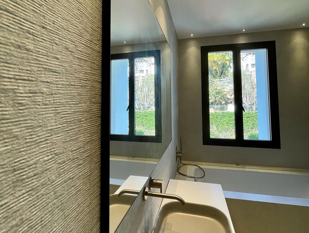 Un baño con lavabo, espejo y dos ventanas.