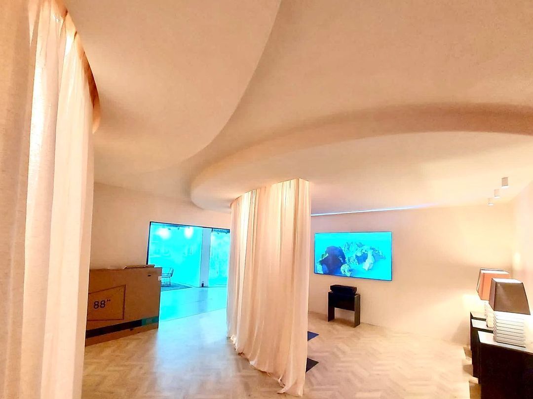 Una habitación con cortinas blancas y un televisor en la pared.