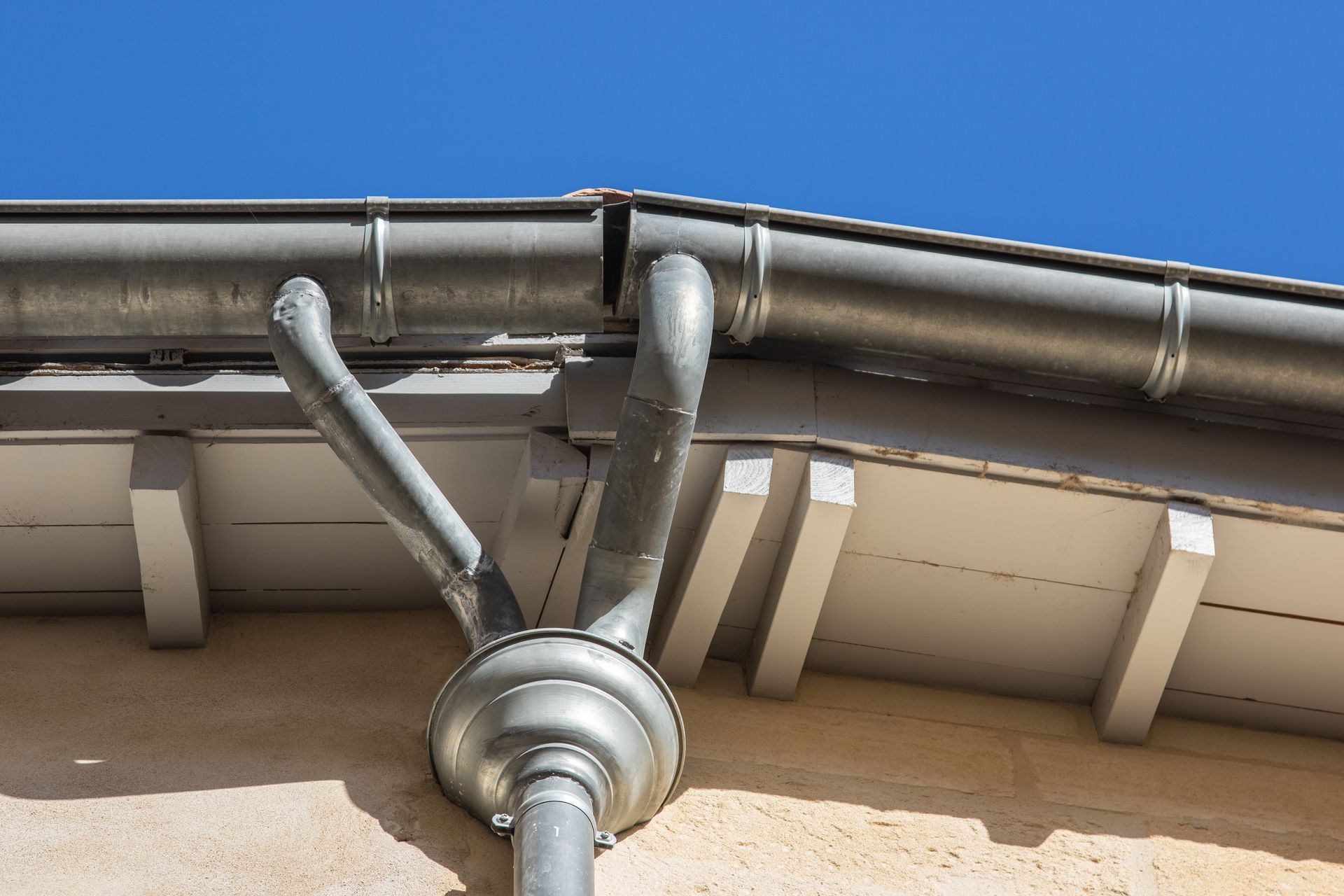 Gouttières en métal gris sur un bâtiment avec un ciel bleu clair en arrière-plan.