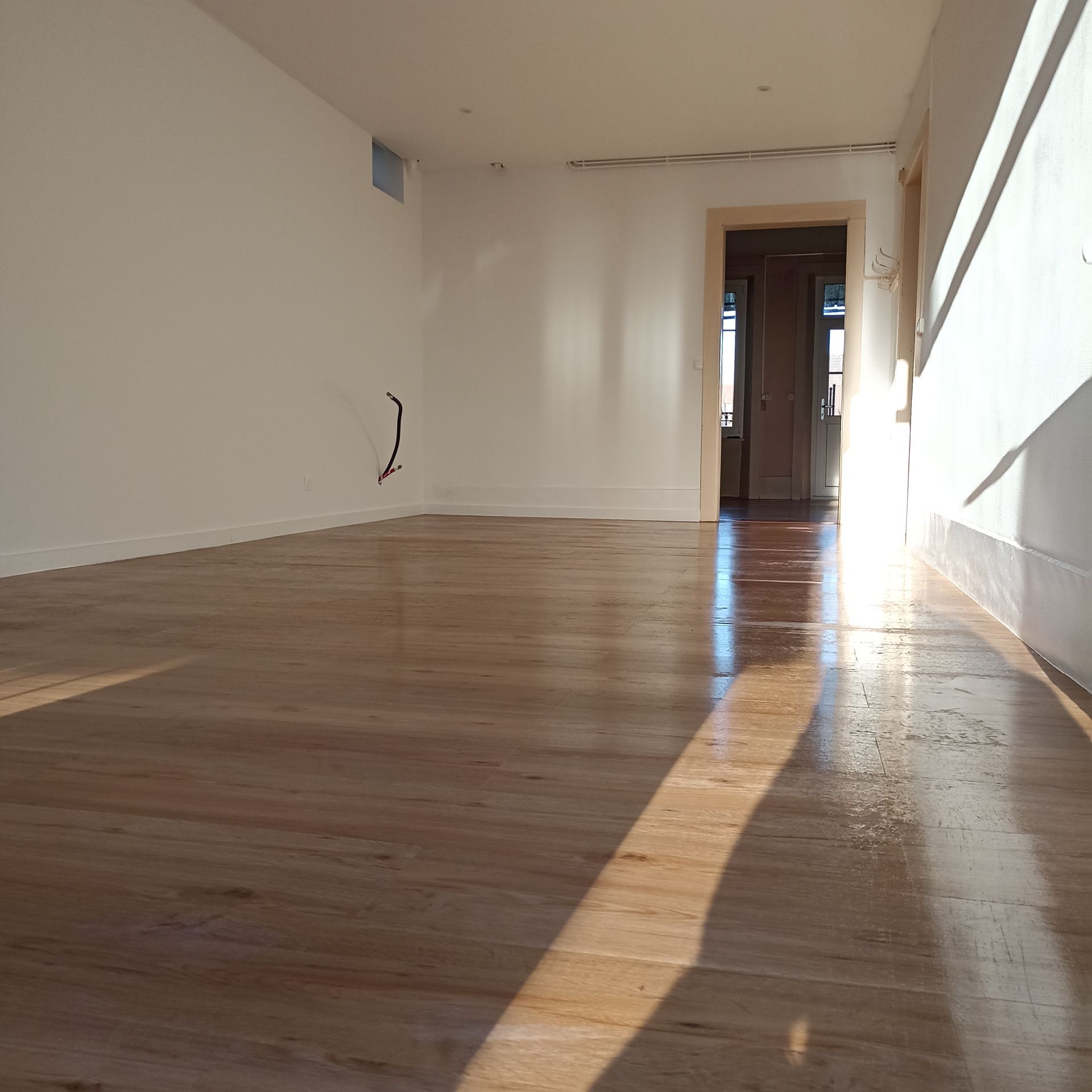 Pièce vide et ensoleillée avec des murs blancs et un parquet ciré
