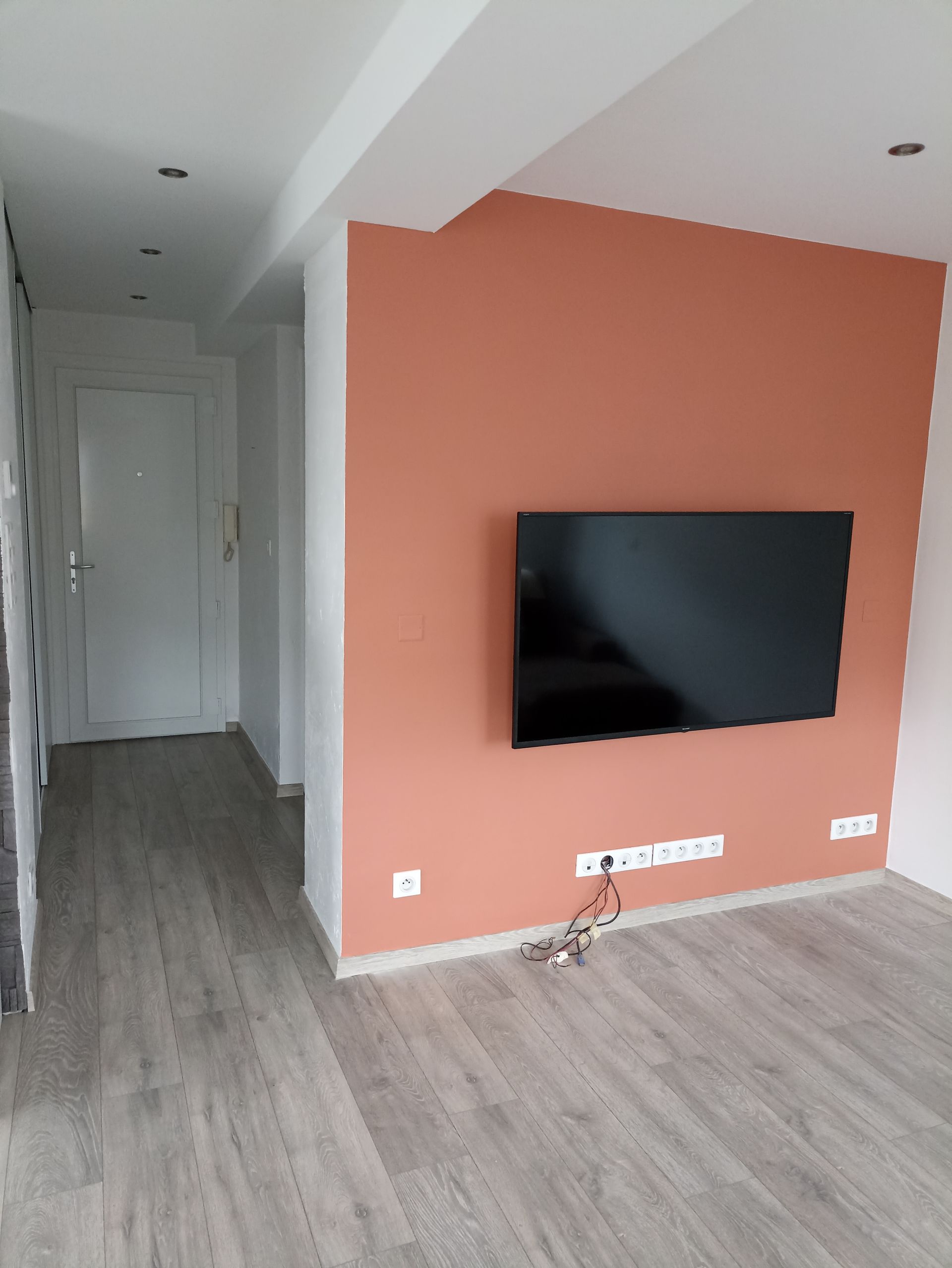 Salon moderne avec un mur d'accent couleur pêche, une télévision murale et un couloir menant à des portes blanches.