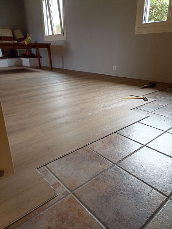 Pièce vide avec parquet clair et une zone partiellement carrelée en terre cuite près de la caméra.