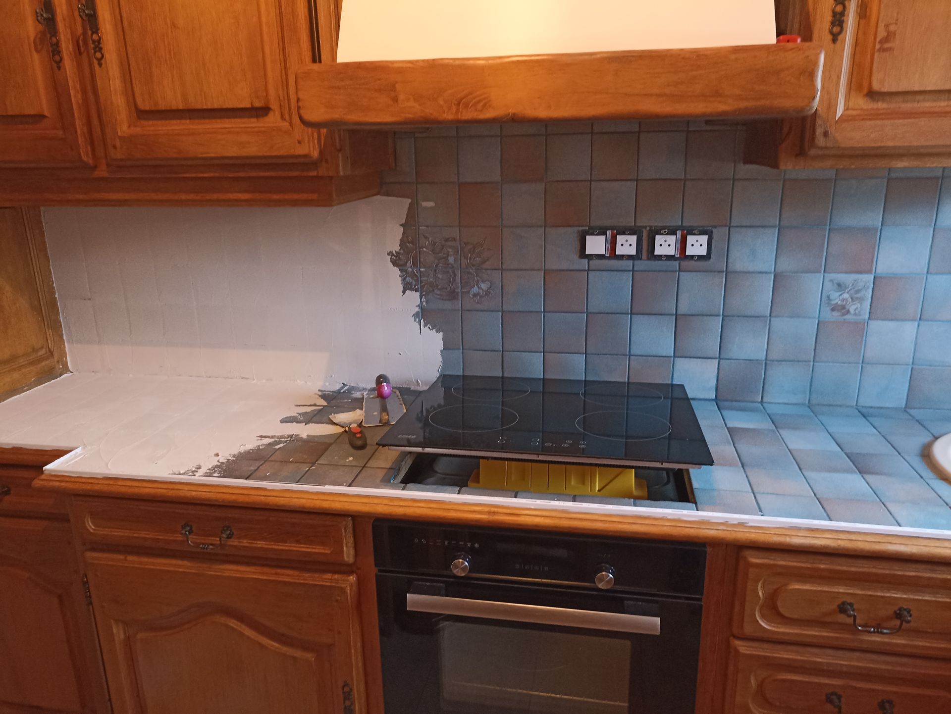 Cuisine en bois avec crédence en carrelage bleu, cuisinière noire et plan de travail blanc avec vaisselle près de l'évier.