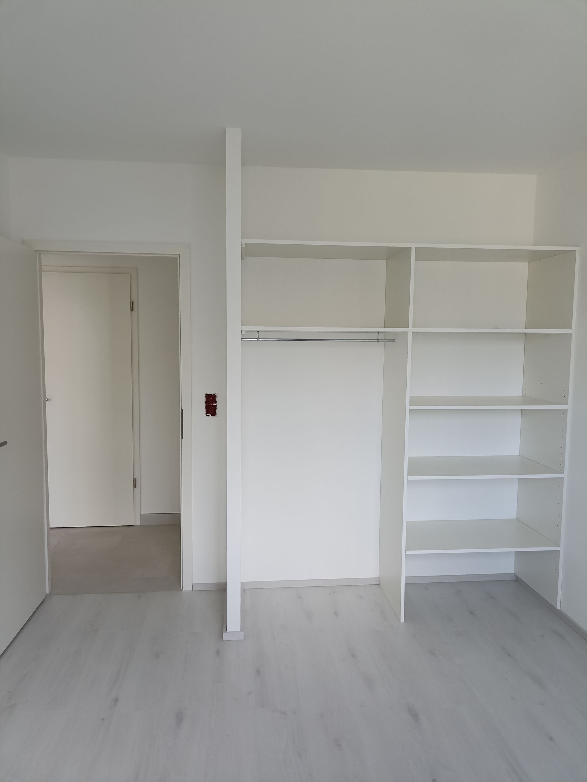 Chambre blanche vide avec placard intégré à étagères ouvertes et une porte donnant sur un couloir
