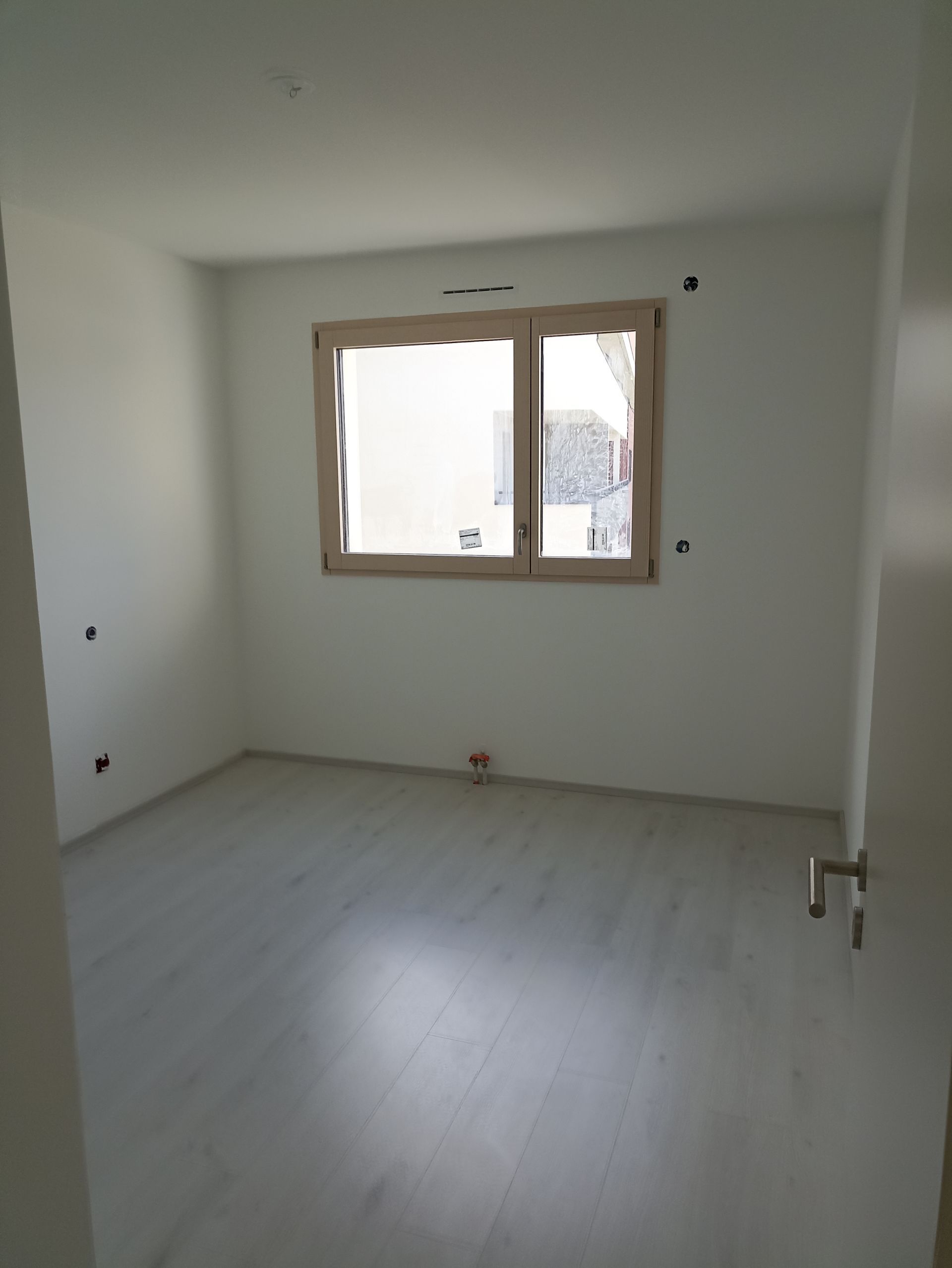 Pièce blanche vide avec parquet clair et une fenêtre sur le mur du fond