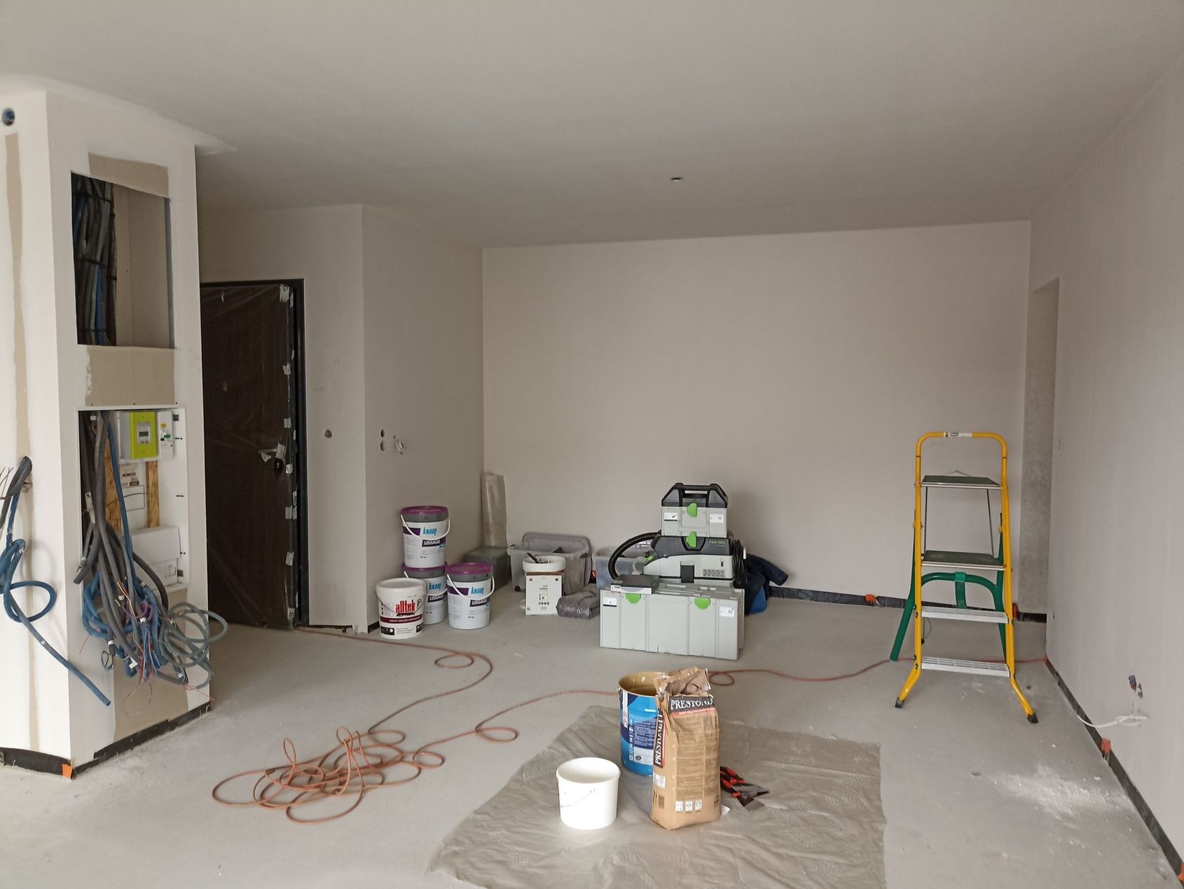 Pièce en travaux avec des seaux de peinture, des outils, des rallonges électriques et un escabeau, en pleine rénovation.