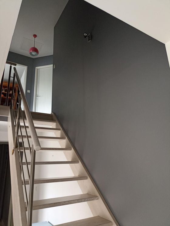 Escalier intérieur avec marches blanches, rampe en métal et murs gris foncé menant à un étage supérieur