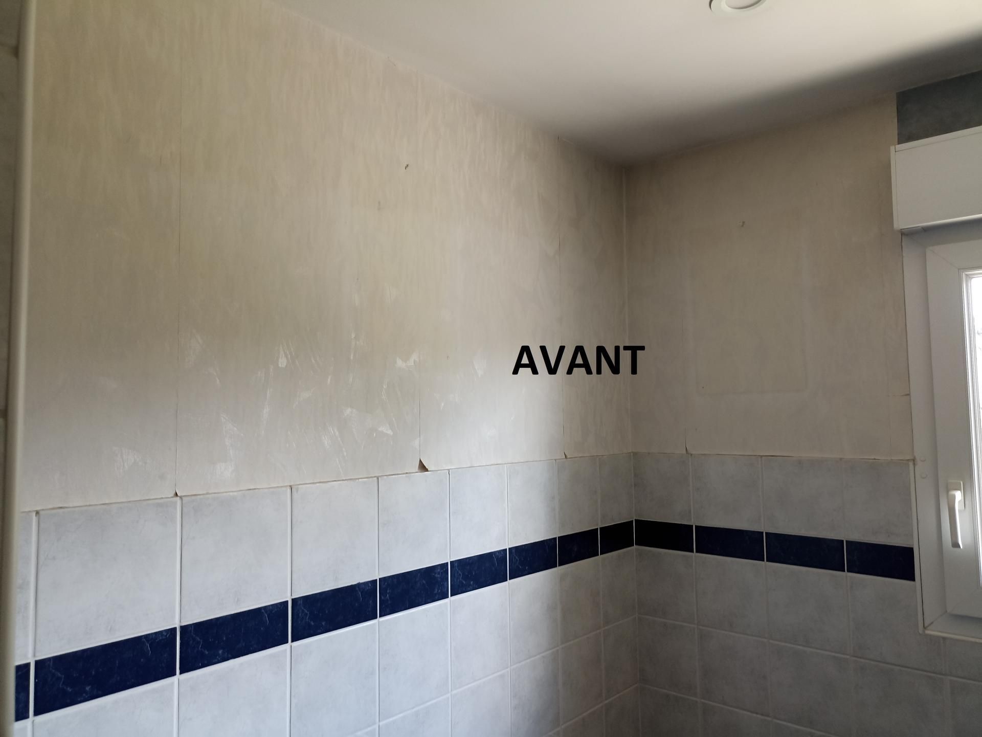 Petit coin de salle de bain carrelé avec des murs beiges et une bordure de carreaux bleus, portant l'inscription « AVANT ».