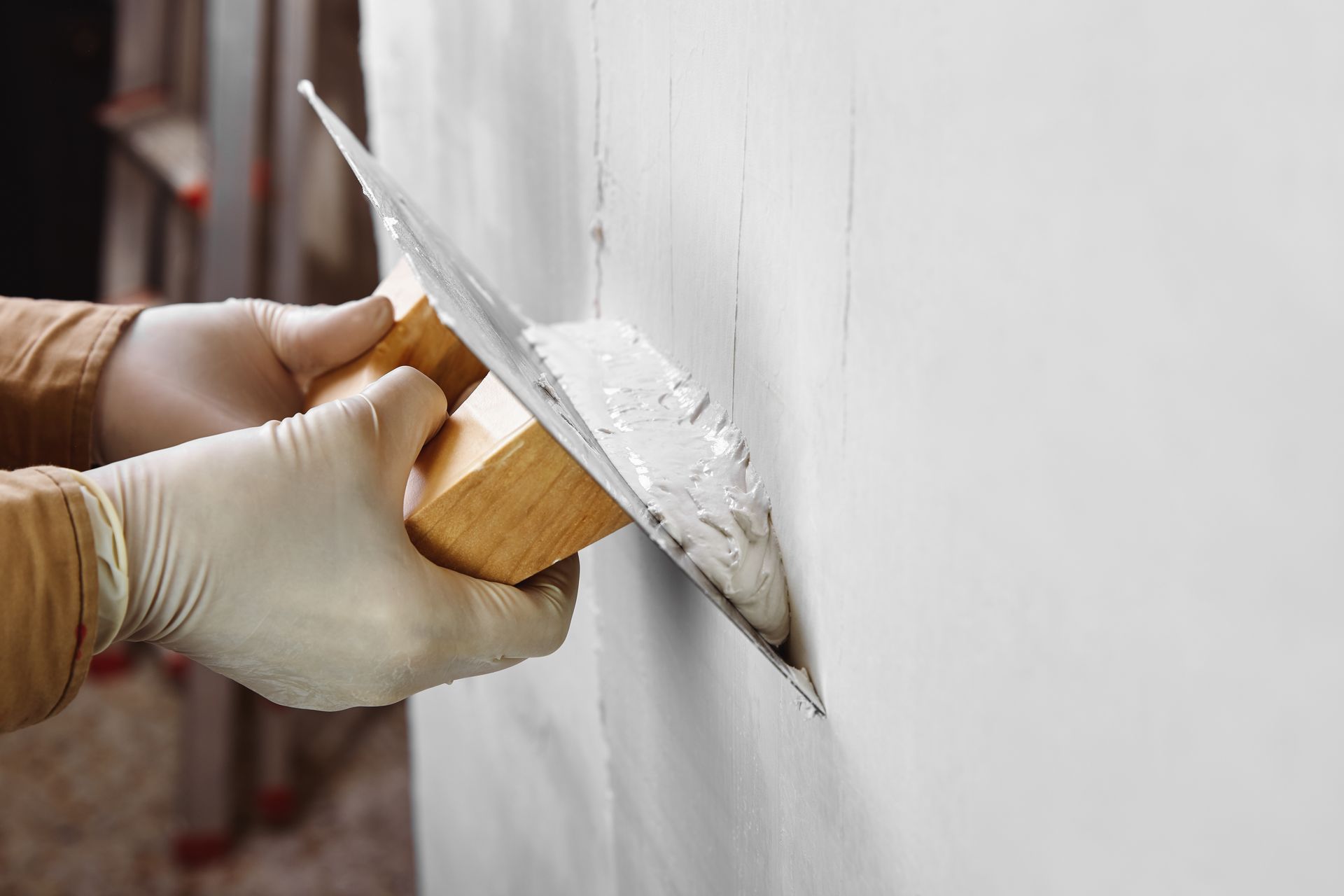 Des mains gantées appliquent du plâtre blanc à la truelle sur un mur lors de travaux de réparation