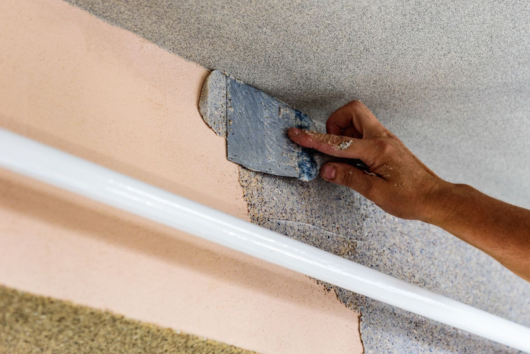 Grattage et lissage manuels d'un enduit gris sur un mur couleur pêche à l'aide d'un couteau à mastic